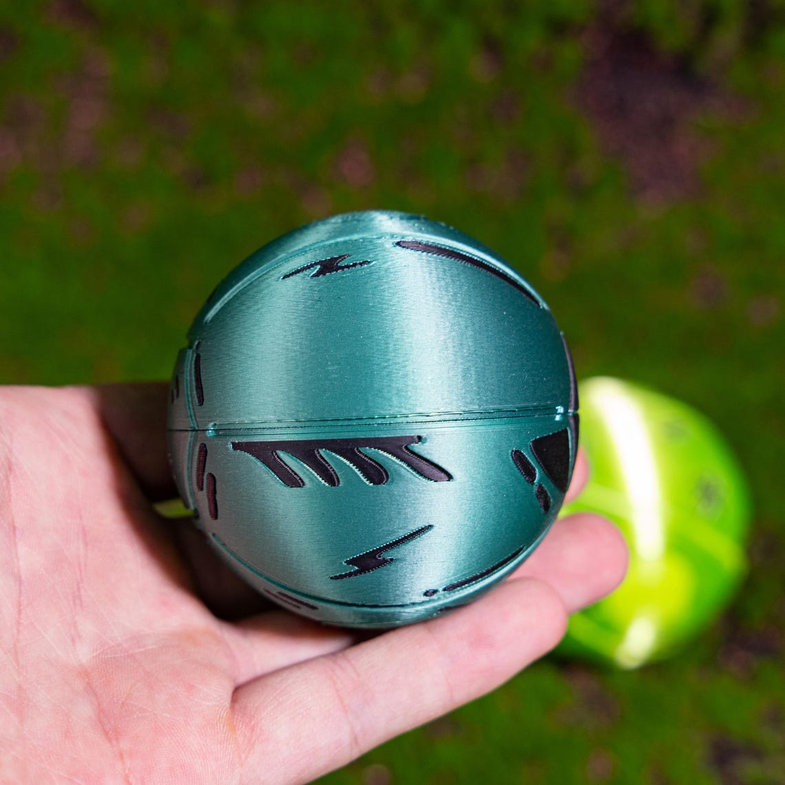 May include: A teal green sphere with black geometric designs. The sphere is made of a smooth, shiny material.