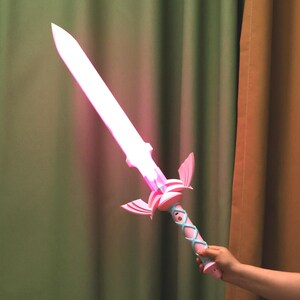 Puede incluir: Una espada de pl&aacute;stico rosa y azul con una funci&oacute;n de iluminaci&oacute;n. La espada tiene un dise&ntilde;o decorativo con alas y un mango con un patr&oacute;n trenzado.