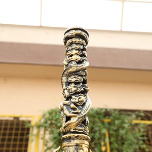 May include: Ornate, gold-colored metal pillar with intricate carvings. The pillar features a repeating cloud design and a dragon wrapped around the column. The top and bottom of the pillar have decorative detailing. The pillar is likely part of a larger decorative structure.