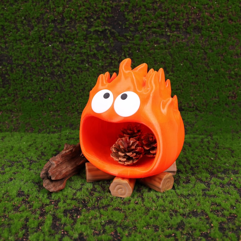 Studio Ghibli-themed Calcifer fire demon organizer for desk storage displayed on a wooden tabletop next to a laptop and stationery. The design captures Calcifer’s playful expression with bright colors and smooth 3D printed detailing. Perfect for organizing small items at home or the office, this Howl’s Moving Castle-inspired decor adds a magical touch to your workspace while serving as a thoughtful gift for Miyazaki fans.
