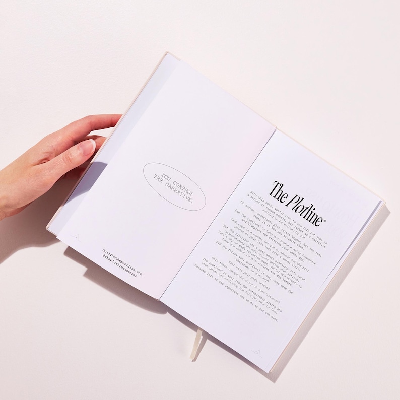 以下が含まれることがあります： 「The Plotline」と「You control the narrative.」というテキストが書かれた白いジャーナルが開かれています。ジャーナルは、プロットと自分のストーリーを作成する方法について書かれたページを開いています。