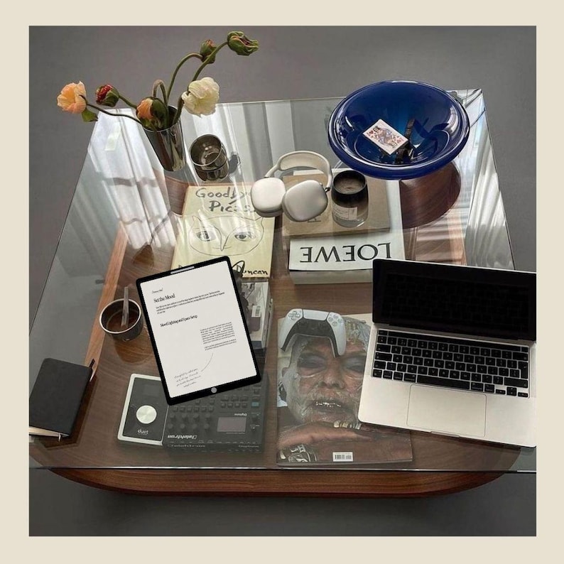 May include: A glass table top with a laptop, a book, a magazine, a wireless controller, a pair of headphones, a book, a small blue bowl, and a book with the text "LOEWE" on it.