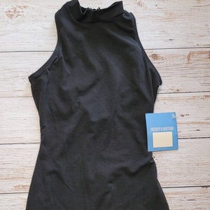 May include: A black sleeveless bodysuit with a mock neck collar. The one-piece garment has a fitted silhouette and short legs. A blue tag is attached to the bodysuit. The bodysuit is displayed on a light wood grain surface.