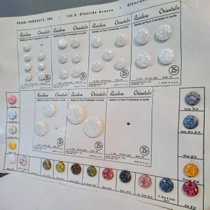 May include: A vintage display card from Pearl Products, Inc. featuring various sizes and colors of Rainbow Oriental mother-of-pearl buttons embedded in lucite. The card includes printed text, style numbers, and pricing labels for each button set.