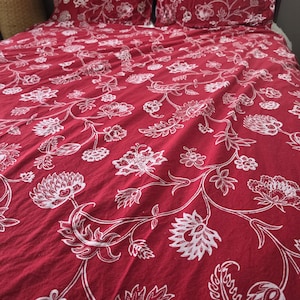 May include: A deep red bedding set featuring a white floral pattern with intricate botanical details. The set includes a large duvet cover and two matching rectangular pillowcases, all decorated with a continuous vine and flower motif.