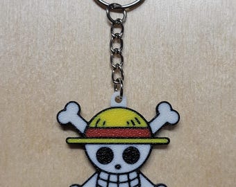May include: A white skull and crossbones keychain with a yellow and red straw hat. The keychain is attached to a silver chain and ring.