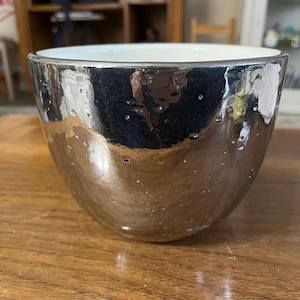 May include: A white ceramic mug with a black handle and the text "But First, Coffee" in a bold, black font. The mug is sitting on a wooden surface. The mug is approximately 4 inches tall.