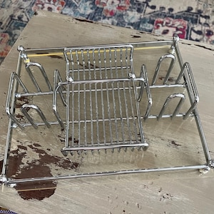May include: A chrome-plated dish rack with multiple compartments for plates, cups, and utensils. The rack has a rectangular base and a grid-like design, ideal for kitchen organization.