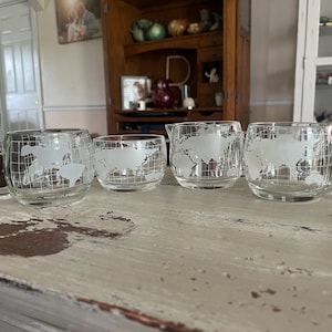 May include: A set of four clear glass drinkware pieces with a world map design. The set includes two mugs with handles, a small creamer, and a small tumbler. The world map is etched in white.