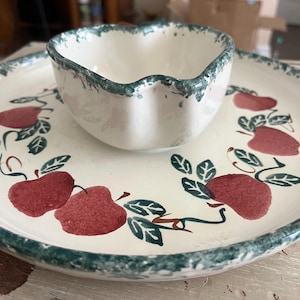 May include: A white ceramic chip and dip set with a green rim and apple design. The set includes a small bowl and a larger plate, perfect for serving snacks at a gathering.