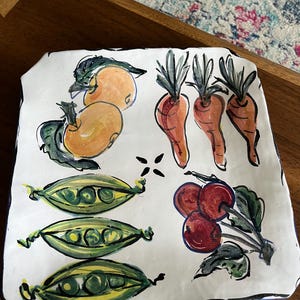 May include: A white ceramic serving platter with hand-painted illustrations of oranges, carrots, peas, and radishes. The platter has a black border and a blue trim, perfect for serving appetizers or small dishes.