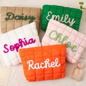 May include: Five quilted pouches in various colors: tan, green, white, pink, and orange. Each pouch features a different name embroidered in a contrasting color: Daisy, Emily, Sophia, Chloe, and Rachel. The pouches are arranged on a light-colored surface.