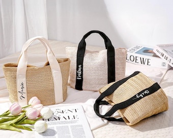 May include: Three personalized straw tote bags with black and white accents. The bags have names printed on them: "Marie", "Kristina", and "Becky". The bags are on a white surface with flowers and a magazine.
