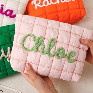 May include: A collection of quilted cosmetic bags in various colors, each embroidered with a name. The bags are in white, orange, green, and pink. The pink bag has the name "Chloe" in green yarn. The bags are rectangular with a quilted pattern.