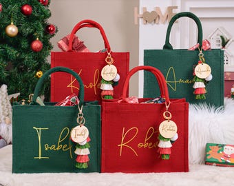 May include: Four tote bags in red and green, with gold lettering and matching handles. Each bag has a wooden charm with a name and tassel. The bags are decorated for the holidays, with a Christmas tree in the background.