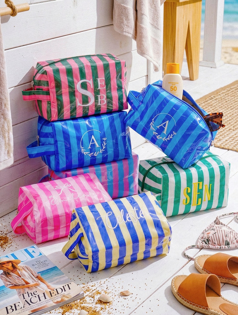 May include: A collection of rectangular, striped toiletry bags in various colour combinations including pink and green, blue and light blue, and yellow and blue. Each bag features a zippered closure, a side handle, and personalised lettering.