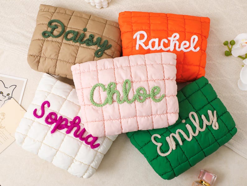 May include: Five quilted pouches in various colors: tan, orange, pink, white, and green. Each pouch features a different name embroidered in a contrasting color: "Daisy", "Rachel", "Chloe", "Sophia", and "Emily".