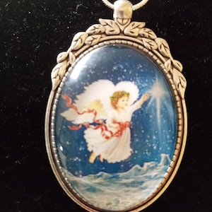 May include: Silver pendant necklace with an oval-shaped glass cameo featuring a white angel with a red sash flying through a blue starry sky.