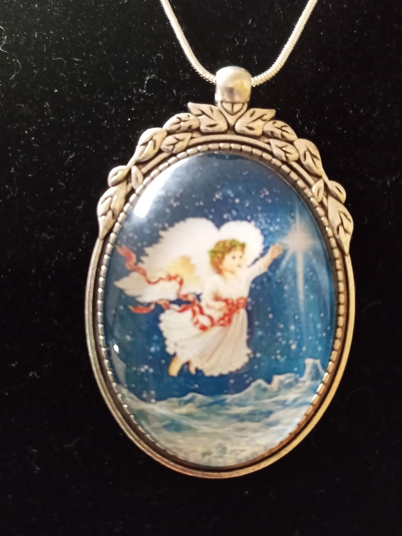 May include: Silver pendant necklace with an oval-shaped glass cameo featuring a white angel with a red sash flying through a blue starry sky.