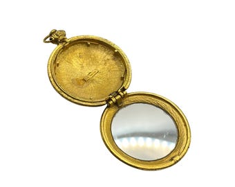 Reloj de bolsillo compacto estilo vintage Max Factor con relieve floral y diseño de pájaro en tono dorado.