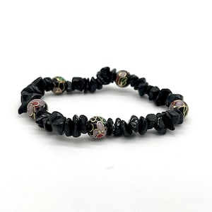 May include: A black stone bracelet featuring four decorative, round beads. The beads are gold with colourful floral designs in red, pink, green, and purple. The bracelet is on a white background.