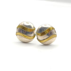May include: Two silver-toned stud earrings with a gold-colored band wrapping around each. The earrings are spherical and have a polished finish. The gold bands add a contrasting accent to the silver base.