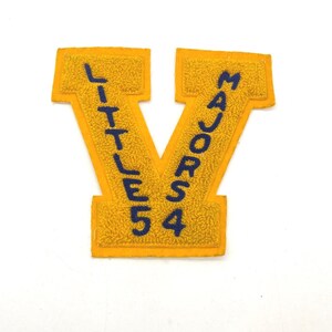 May include: A yellow felt letter "V" patch with blue text. The left side reads "LITTLE 5" and the right side reads "MAJORS 4". The patch has a textured, fuzzy appearance and is likely for a varsity jacket or similar apparel.