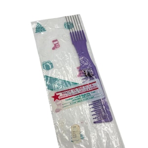 May include: A new, purple comb in a clear plastic package decorated with festive symbols. The packaging includes a label stating "MADE IN THE U.S.A. WITH QUALITY, VALUE & PRIDE."