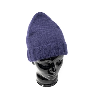May include: A dark purple knit beanie cap with a ribbed cuff at the base. The hat features a soft, textured wool-like material and a pointed crown shape, displayed on a glossy black mannequin head against a plain white background.