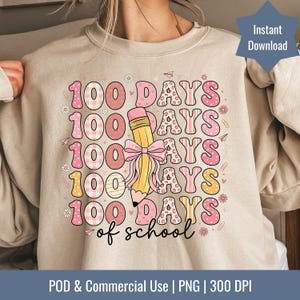 Puede incluir: Sudadera beige con un gráfico colorido que celebra los 100 días de escuela. El diseño presenta el texto "100 DAYS of school" en rosa, amarillo y blanco, junto con un lápiz y elementos decorativos. Las palabras "Instant Download" también son visibles.