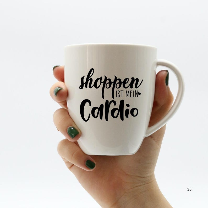 K&ouml;nnte beinhalten: Wei&szlig;e Keramiktasse mit einem schwarzen Design, auf dem "shoppen ist mein Cardio" steht, was &uuml;bersetzt "Shoppen ist mein Cardio" bedeutet.