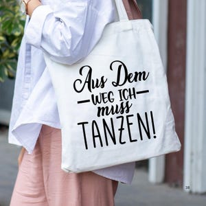 K&ouml;nnte beinhalten: Eine wei&szlig;e Einkaufstasche mit schwarzem Text, der "Aus Dem -Weg Ich- muss TANZEN!" lautet.
