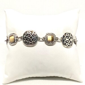 May include: A silver-tone link bracelet featuring alternating square and rectangular stations. Two stations display an openwork scroll pattern, while the other two feature a smooth, brushed gold-tone center framed by small, clear, sparkling stones.