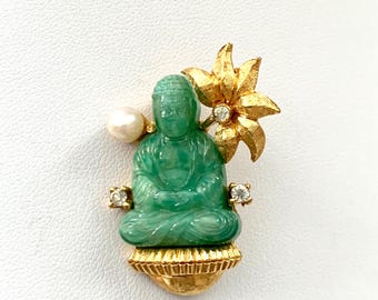 May include: A green jade Buddha figurine with a gold flower and pearl accents. The Buddha is sitting on a gold base.