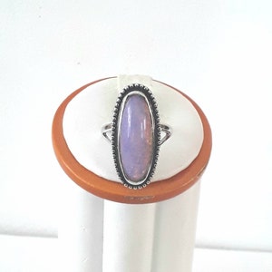 May include: A silver ring with a light purple oval-shaped gemstone set in a bezel setting. The ring is on a display stand.
