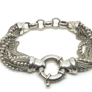 May include: A silver bracelet with multiple chain links and a round clasp. The bracelet is made of a delicate, interwoven chain design.