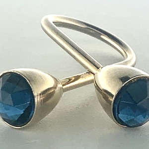 May include: A pair of gold-toned cufflinks with faceted, deep blue gemstone accents. The cufflinks have a classic design, featuring a rounded shape with a connecting bar. The gemstones are set within the gold metal, creating a sophisticated look.