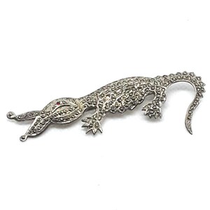 May include: A silver lizard brooch with a red rhinestone eye. The lizard is covered in small, sparkling stones.