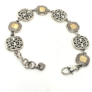 May include: A link bracelet featuring alternating square charms. Four charms display an intricate silver filigree scrollwork pattern, while three charms feature a smooth, polished gold-tone center framed by a silver beaded border. A heart-shaped charm hangs near the lobster claw clasp.