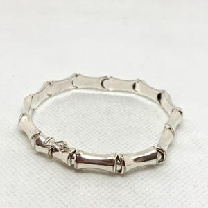 May include: A polished silver bracelet featuring a series of connected segments designed to resemble bamboo stalks. The circular piece includes a small, integrated metal clasp mechanism that secures the links together in a continuous loop.