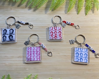 May include: Four keychains with clear square photo charms featuring a group of people. Each keychain has a silver charm with a house shape and a letter bead spelling "HS". The charms are attached to silver key rings with colorful letter beads.