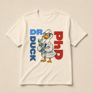 Op de afbeelding: Een crèmekleurig T-shirt met korte mouwen en een cartoon-eend met een bril en een witte doktersjas. De eend houdt een kleurrijke DNA-streng vast. De tekst DR DUCK staat in het blauw aan de linkerkant en de tekst PHD in het rood aan de rechterkant.