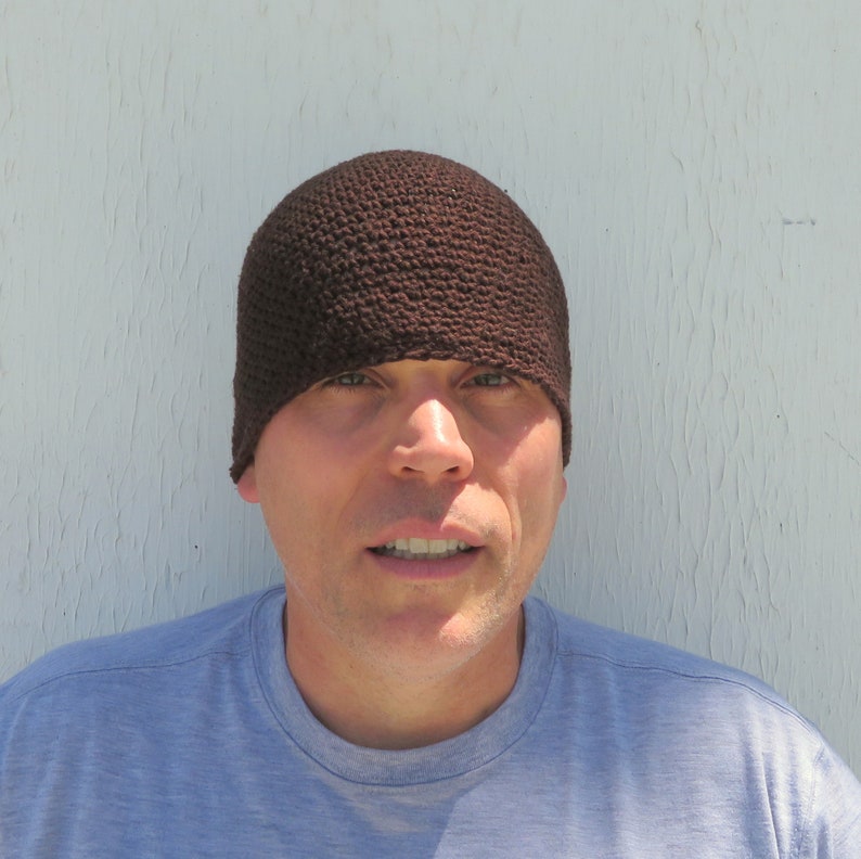 The model is wearing a dark brown, crocheted beanie that fits snugly and covers his ears.