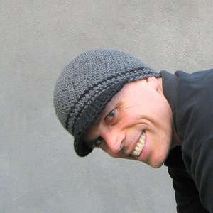 The model is wearing a grey, crocheted beanie with a brim...there are two stripes of black near the bottom of the hat and the brim is also black- the hat fits snugly and almost covers his ears.