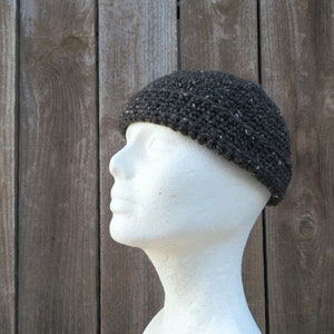May include: A dark gray crocheted beanie hat with a textured surface. The hat is on a white mannequin head.