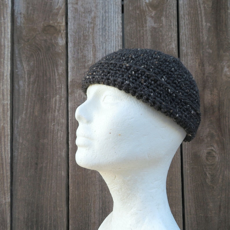 May include: A dark gray crocheted beanie hat with a textured surface. The hat is on a white mannequin head.