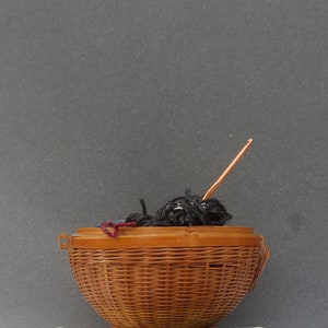 May include: A brown wicker basket filled with black yarn and a copper crochet hook.
