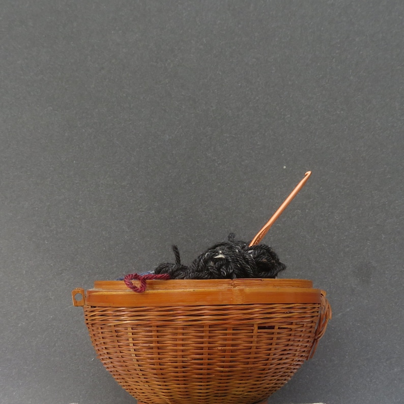 May include: A brown wicker basket filled with black yarn and a copper crochet hook.