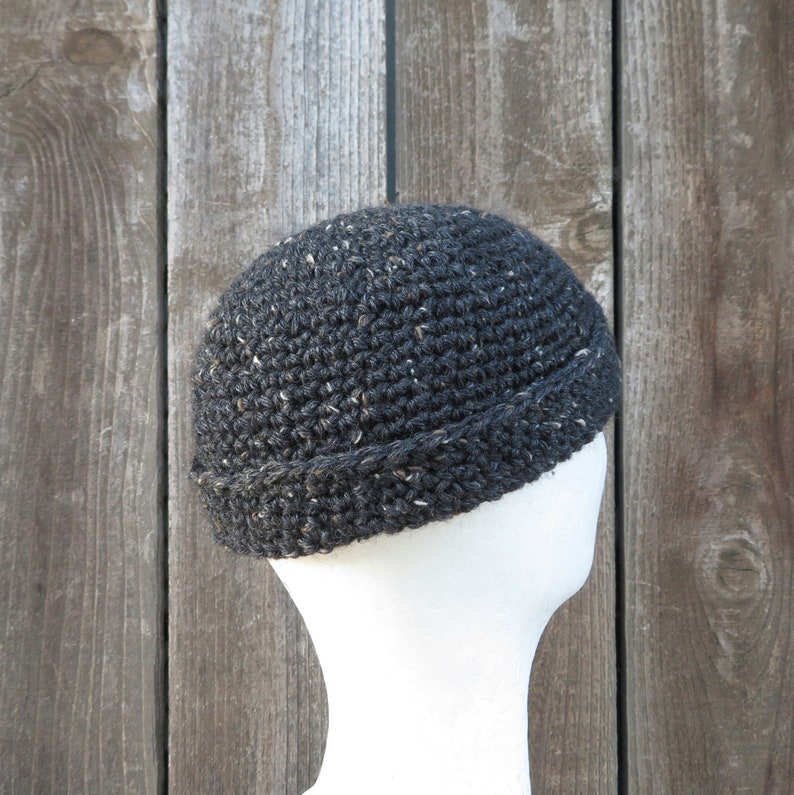 May include: A black crocheted beanie with a flecked texture. The beanie has a turned-up brim.