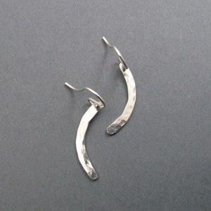 May include: A pair of silver earrings with a hammered finish and a curved shape. The earrings are made of metal and have a simple, elegant design.